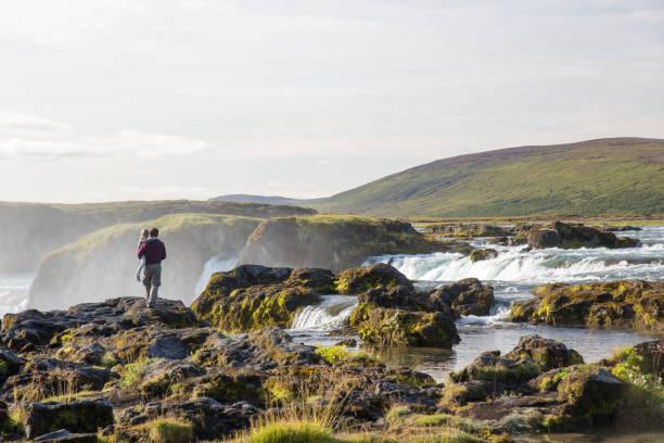 A father holding his daughter and looking at the Godafoss Waterfall in Iceland.