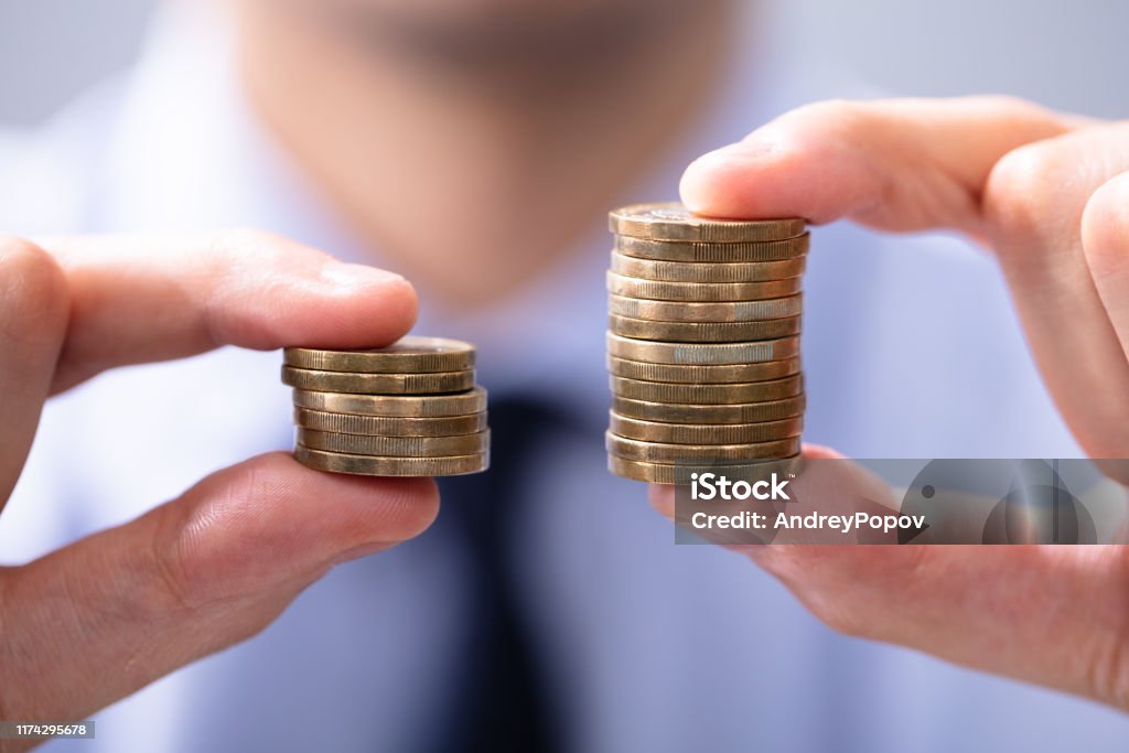 Man Comparing Two Coin Stacks Man Holding Two Coin Stacks To Compare Wages Stock Photo