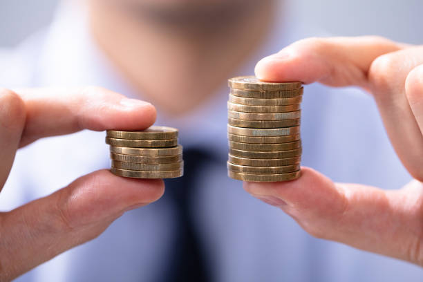 Man Comparing Two Coin Stacks Man Holding Two Coin Stacks To Compare salary stock pictures, royalty-free photos & images