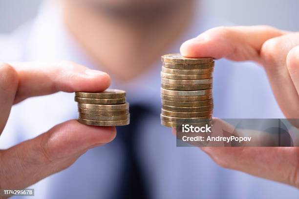 Man Comparing Two Coin Stacks Stock Photo - Download Image Now - Wages, Growth, Comparison