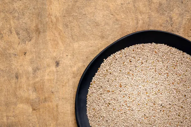 organic white chia seeds rich in omega-3 fatty acids,  top view of a black plate against textured bark paper