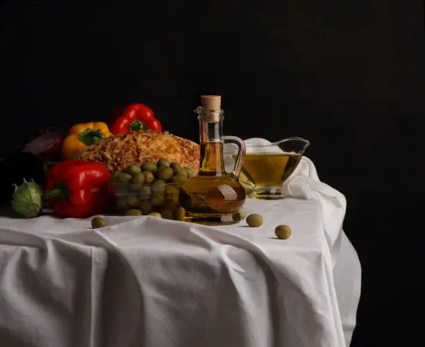 Photo of Pitcher of olive oil, vase of olives and fruit on dark background