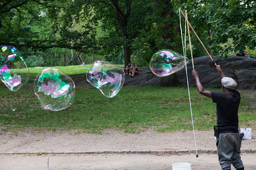 New York, USA - July 27, 2019. A black man playing with soap bubbles in the Central Park of New York City, USA