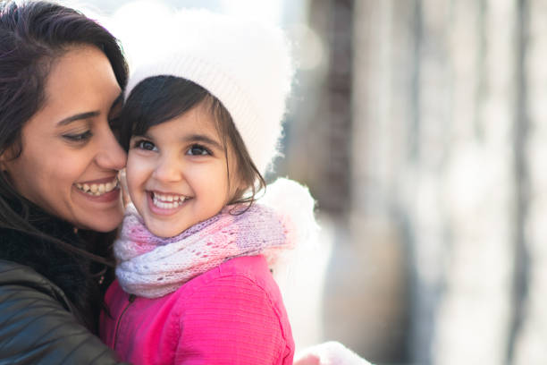 Smiling Muslim mother and child A beautiful young Muslim mother bonds with her daughter one winter afternoon. They are dressed warmly and are smiling while the mother embraces the girl in a loving hug. north african ethnicity stock pictures, royalty-free photos & images