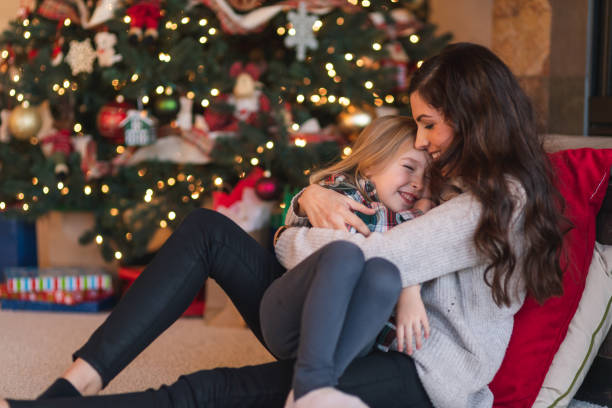 istock Mom snuggles with her daughter by the Christmas tree 1174331183