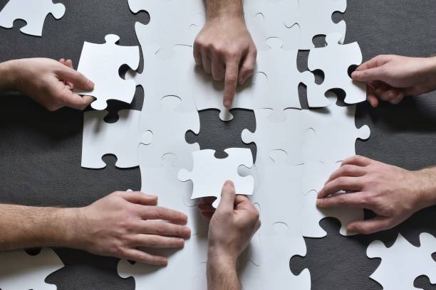 Cropped Hands Of People Arranging Jigsaw Puzzles On Table
