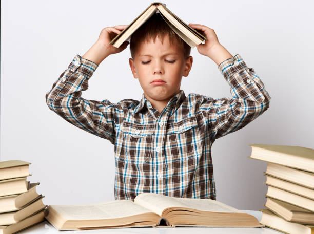 istock Tired school boy doing homework at desk over white background. 1174399068