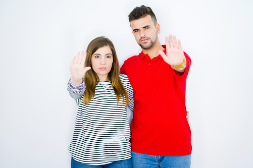 Young beautiful couple hugging together over white isolated background with open hand doing stop sign with serious and confident expression, defense gesture