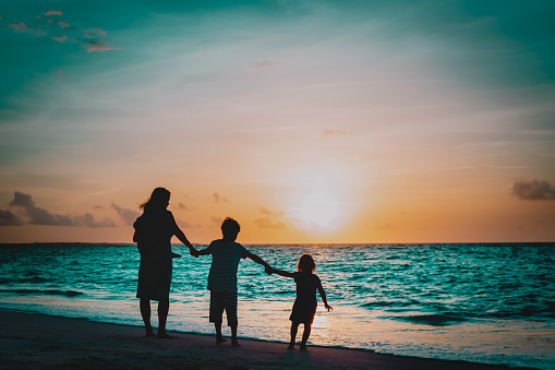 mother with three kids walking on beach at sunset, family on vacation