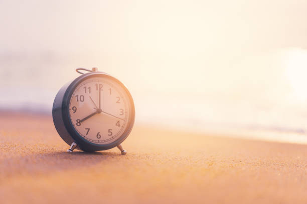 istock Clock on sand beach in morning suns light with smooth wave background. 1174401586