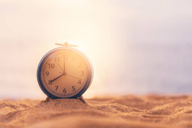 istock Clock on sand beach in morning suns light with smooth wave background. 1174401590