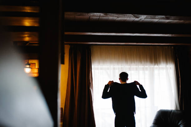 istock A handsome confident young man standing in a white shirt and dressed jacket. Handsome man standing back near window and looking away. 1174403059