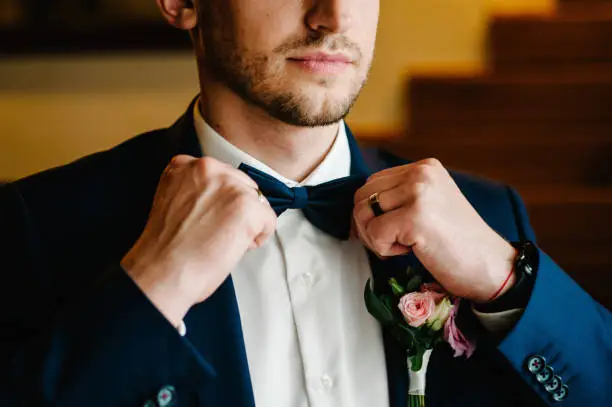 Photo of Man in a suit correcting his bow-tie. Morning preparation groom at home. Fashion photo of a man.