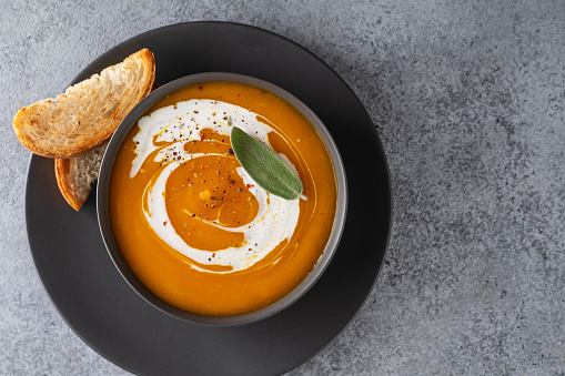Pumpkin soup with sage on grey background. Copy spase.