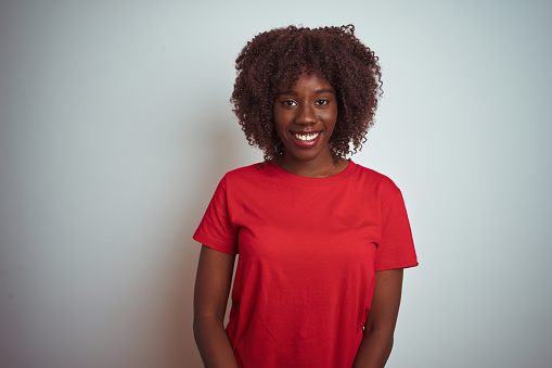Young african afro woman wearing red t-shirt over isolated white background looking away to side with smile on face, natural expression. Laughing confident.