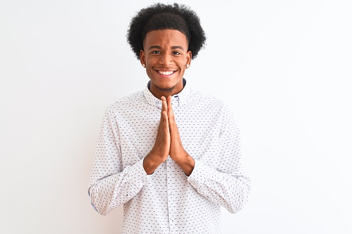 Young african american man wearing elegant shirt standing over isolated white background praying with hands together asking for forgiveness smiling confident.