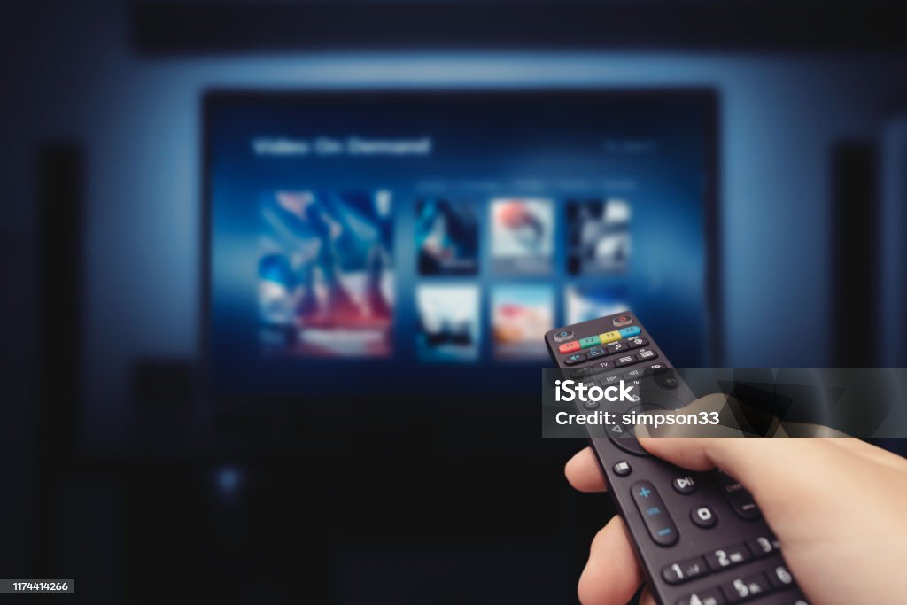 VOD service screen with remote control in hand VOD service screen with remote control in hand. Video On Demand television internet stream multimedia concept Television Set Stock Photo