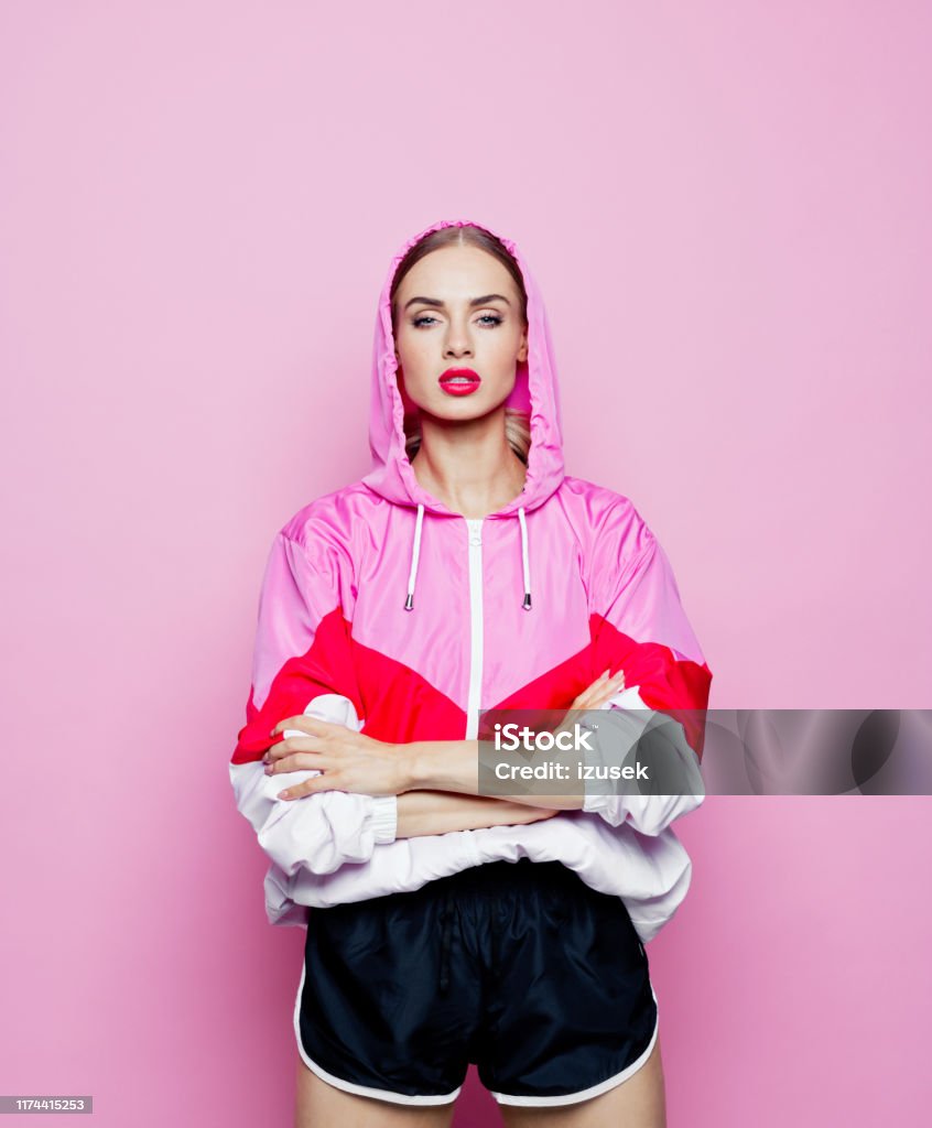 Fashion portrait of beautiful woman in tracksuit against pink background Mid adult beautiful woman wearing oversized tracksuit and shorts standing against pink background, looking at camera. Fashion Stock Photo