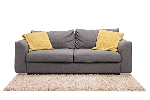 Studio shot of a grey sofa with green pillows on a carpet isolated on white background