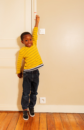 Little black boy stretch his hand to measure height on door at home
