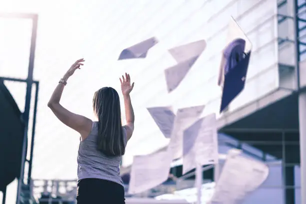 Photo of Business woman throwing work papers in the air. Stress from workload. Person going home or leaving for vacation. Employee got fired. Job or project done. Difficult workday over.