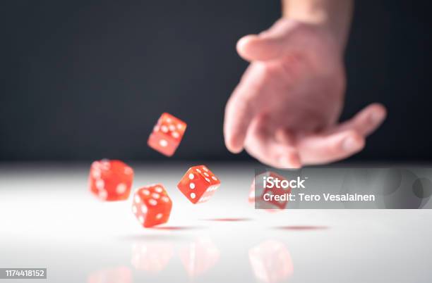 Hand Throwing And Rolling Dice Gambler Tossing Five Red Poker And Casino Dice On Table Man Gambling Or Playing Board Game Stock Photo - Download Image Now