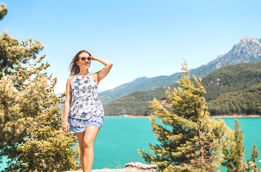 Woman walking in nature, mountain in the background. Adventure, freedom and carefree lifestyle. Millennial lady in summer dress. Landscape with valley, lake and forest. Candid smiling happy person.