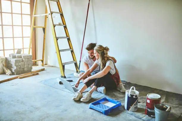 Shot of a young couple using a laptop while busy with renovations at home