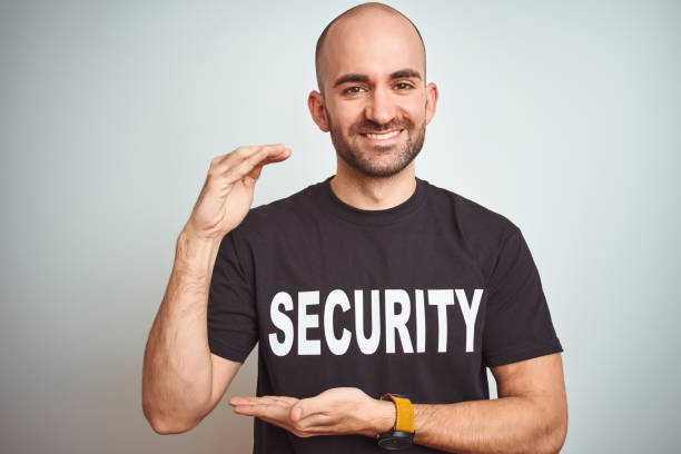 istock Young safeguard man wearing security uniform over isolated background gesturing with hands showing big and large size sign, measure symbol. Smiling looking at the camera. Measuring concept. 1174421100