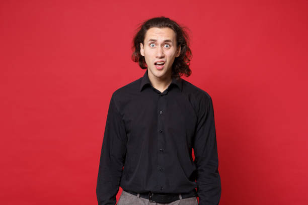 Young sad curly long haired man in black shirt standing posing isolated on red background studio portrait. People sincere emotions lifestyle concept. Mock up copy space. Problem crisis depression joven triste hombre rizado de pelo largo en camisa negra de pie posando aislado en la pared roja fondo retrato de estudio. personas emociones sinceras concepto de estilo de vida. mock hasta espacio de copia. depresión de crisis de problemas
