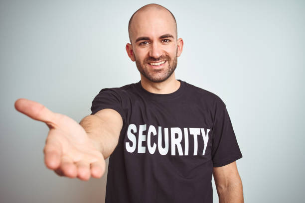 istock Young safeguard man wearing security uniform over isolated background smiling friendly offering handshake as greeting and welcoming. Successful business. 1174421471