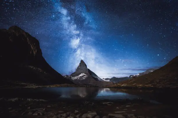 Man exploring the Zermatt area in Switzerland at night - looking at starry sky and Milky Way near the Matterhorn and Riffelsee lake in Gornergrat area - summertime