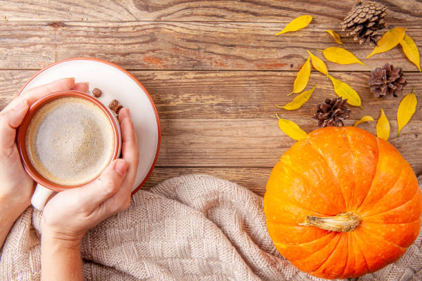 istock Hands holding warm coffee on wooden background with pumpkin 1174424217