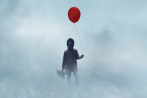 Little girl wearing gas and holding red balloon stands in fog