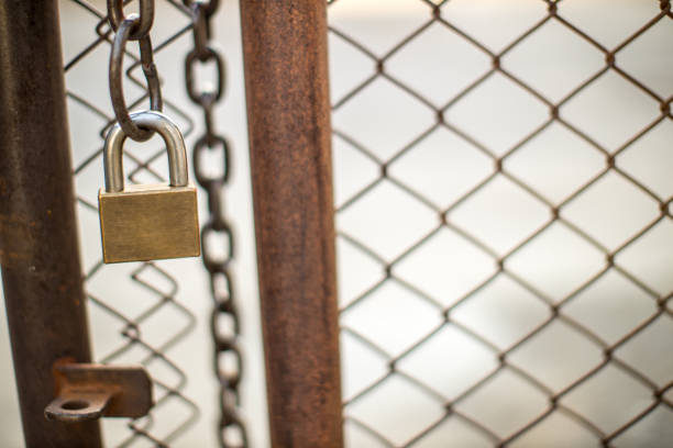 Lock on a chain link security fence. Chicken wire fence gate is locked with a chain and a padlock. padlock and strong steel chain wrapped around the metal entrance gate.