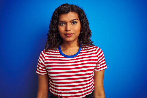 Transsexual transgender woman wearing stiped t-shirt over isolated blue background with serious expression on face. Simple and natural looking at the camera.