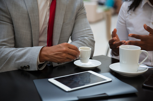 Business partners discussing work issues over cup of coffee. Hands of business people sitting at table with tablet in cafe, drinking coffee, gesturing. Coffee break concept