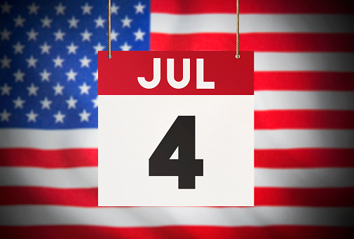 Calendar standing in front of the American flag and showing JUL 4 Stock Image