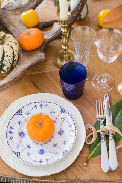 istock Luxurious elegant wedding decor in autumn style. Wooden vintage table setting with ceramic plates and silver cutlery. Fresh flowers in a vase, orange pumpkins, deer horns and candles. Romantic dinner. 1174432409