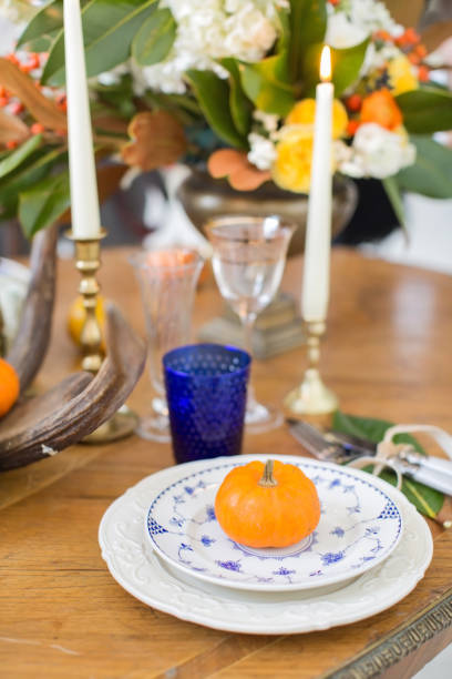 istock Luxurious elegant wedding decor in autumn style. Wooden vintage table setting with ceramic plates and silver cutlery. Fresh flowers in a vase, orange pumpkins, deer horns and candles. Romantic dinner. 1174432427