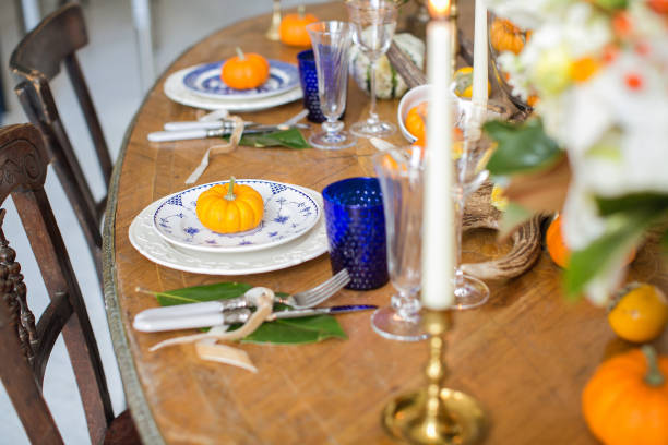 istock Luxurious elegant wedding decor in autumn style. Wooden vintage table setting with ceramic plates and silver cutlery. Fresh flowers in a vase, orange pumpkins, deer horns and candles. Romantic dinner. 1174433035