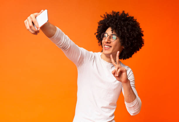 Young black guy making selfie with peace gesture on cellphone
