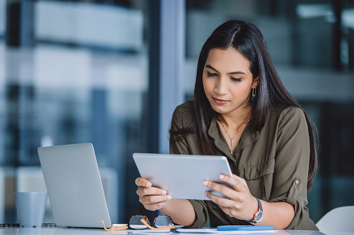 Cropped shot of an attractive young businesswoman sitting alone in her office and using a tablet