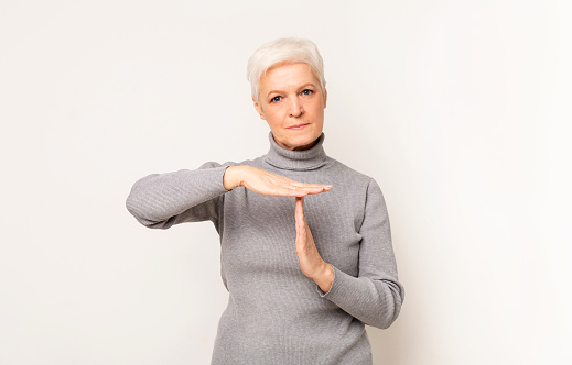 Body language. Impatient senior woman making time out gesture, light studio background with copy space.