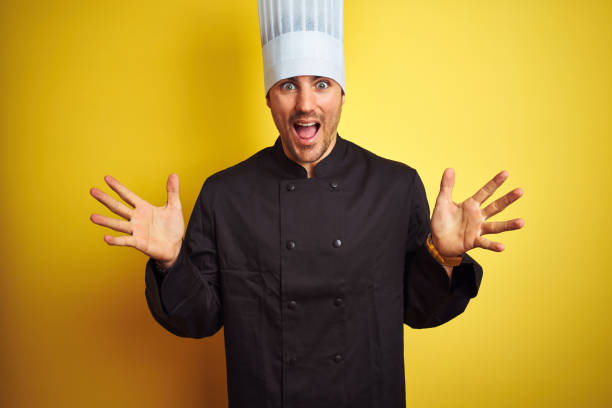 istock Young chef man wearing uniform and hat standing over isolated yellow background celebrating crazy and amazed for success with arms raised and open eyes screaming excited. Winner concept 1174439002