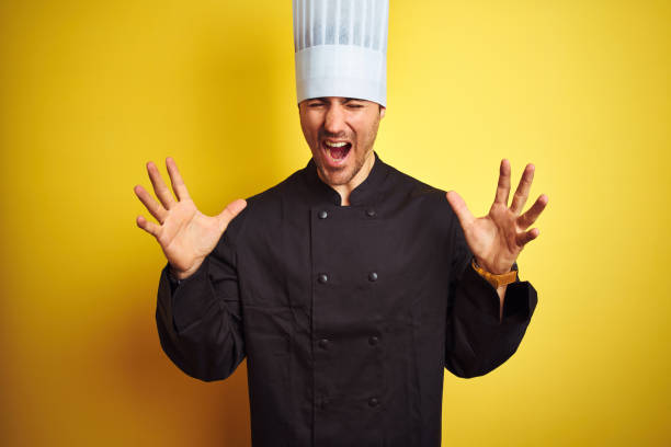istock Young chef man wearing uniform and hat standing over isolated yellow background celebrating mad and crazy for success with arms raised and closed eyes screaming excited. Winner concept 1174439022