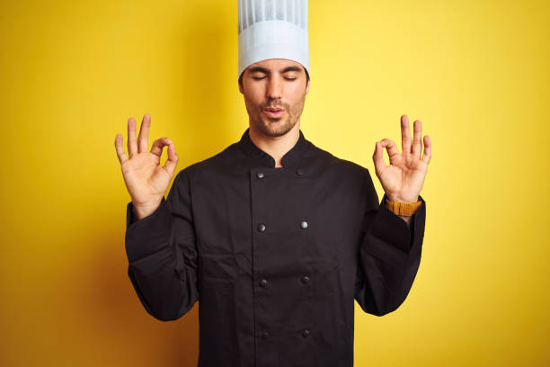 istock Young chef man wearing uniform and hat standing over isolated yellow background relax and smiling with eyes closed doing meditation gesture with fingers. Yoga concept. 1174439827