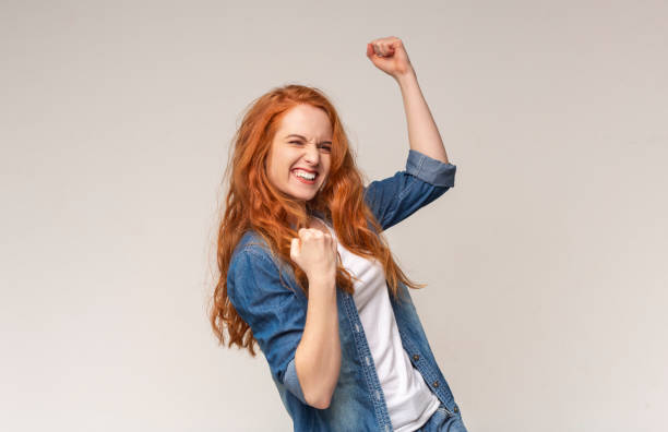 millennial girl shaking fists świętuje sukces na lekkim tle studia - winning success women victory zdjęcia i obrazy z banku zdjęć