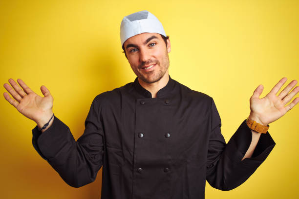 istock Young handsome chef man cooking wearing uniform and hat over isolated yellow background clueless and confused expression with arms and hands raised. Doubt concept. 1174440196