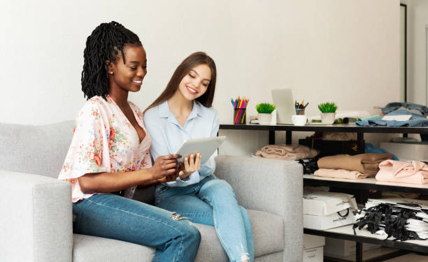 istock Fashion Stylist And Client Using Tablet Sitting On Sofa Indoor 1174441137
